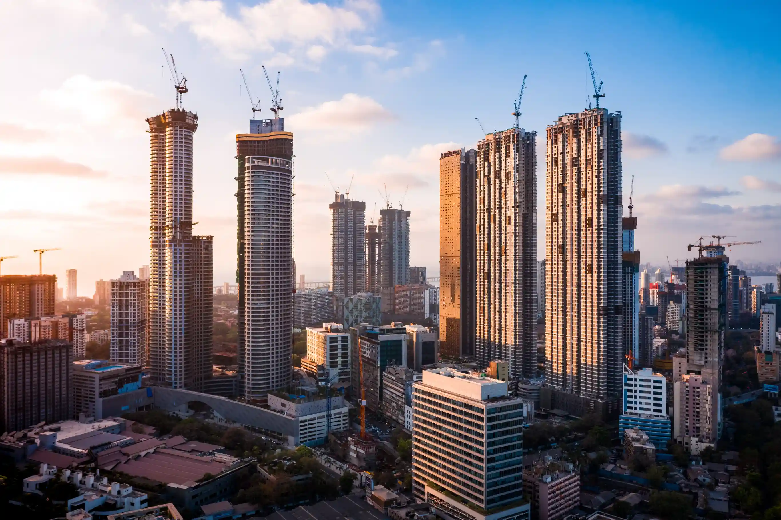 Mumbai high-rise towers under construction at sunrise, cranes visible against a clear blue sky